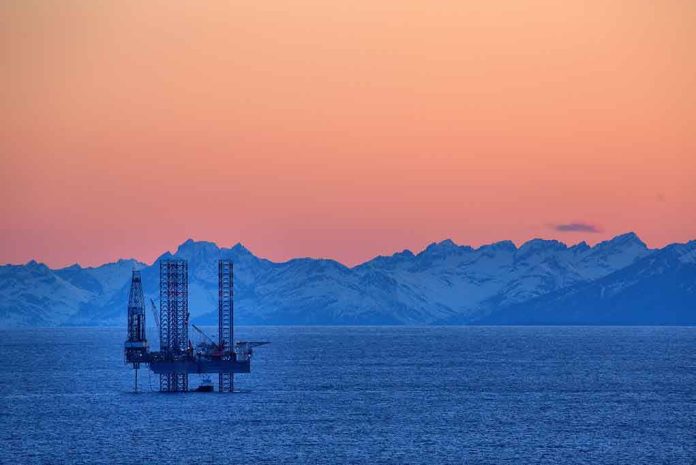 An oil rig in the ocean with a backdrop of mountains during sunset