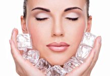 A woman with closed eyes holding ice cubes against her face