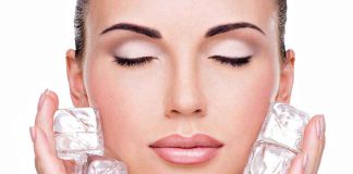 A woman with closed eyes holding ice cubes against her face