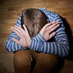A child sitting on the floor with their hands covering their face, expressing distress