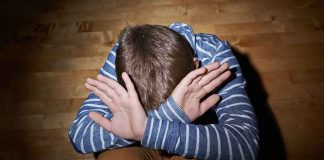 A child sitting on the floor with their hands covering their face, expressing distress
