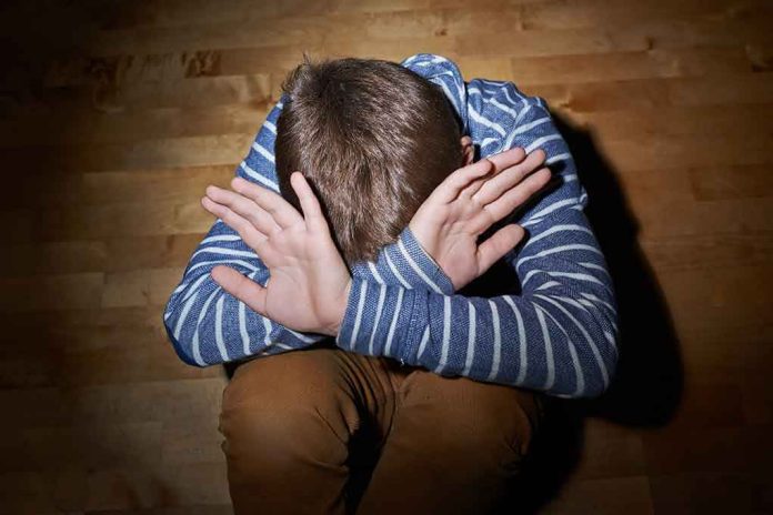 A child sitting on the floor with their hands covering their face, expressing distress