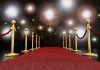 A red carpet lined with gold stanchions and ropes under bright spotlights