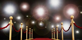 A red carpet lined with gold stanchions and ropes under bright spotlights