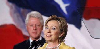 Hillary Clinton delivering a speech with Bill Clinton in the background