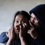 Man holding womans mouth, gesturing silence.