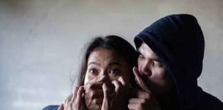 Man holding womans mouth, gesturing silence.