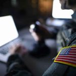 U.S. Military’s SHOCKING “Double Tap” Accusation Soldier using laptop with US flag patch visible.