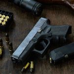 Handgun with ammunition, magazine, and rifle on wooden table.