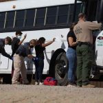 Border patrol officers investigating people near a bus.