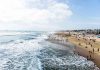 Crowded beach with waves and people enjoying sun.