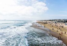Crowded beach with waves and people enjoying sun.