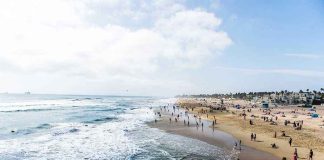 Crowded beach with waves and people enjoying sun.