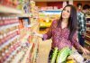 Woman shopping in a grocery store aisle with a cart full of vegetables