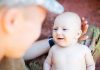 A smiling baby interacting with a parent in a military uniform