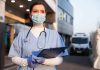 Viral Video Ends Nurse’s Career Nurse in scrubs and mask outside hospital holding clipboard.
