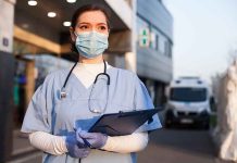 Viral Video Ends Nurse’s Career Nurse in scrubs and mask outside hospital holding clipboard.