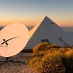 Satellite dish near pyramid-shaped building at sunset.