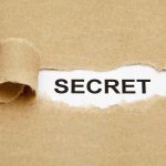 A torn piece of brown paper revealing the word SECRET underneath