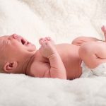 A newborn baby lying on a soft blanket, crying with a distressed expression