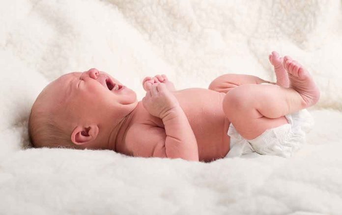 shutterstock_154248668.jpg A newborn baby lying on a soft blanket, crying with a distressed expression