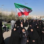 Group of women in black attire marching with an Iranian flag
