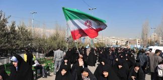 Group of women in black attire marching with an Iranian flag