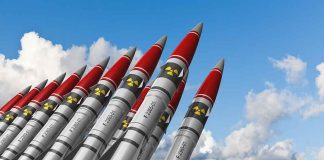 A row of military missiles with red tips and nuclear symbols against a blue sky