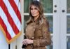 $40M Melania Film Sparks “Bribe” Fury Woman in brown coat beside American flag.