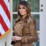 $40M Melania Film Sparks “Bribe” Fury Woman in brown coat beside American flag.