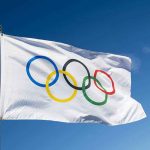 Olympic BETRAYAL: Gold Medalist Trashes America Olympic flag waving against clear blue sky.