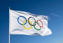 Olympic flag waving against clear blue sky.