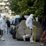 Investigators in hazmat suits carrying equipment cases.