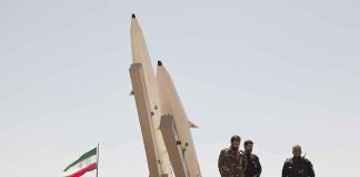 Military personnel beside missiles and Iranian flag.