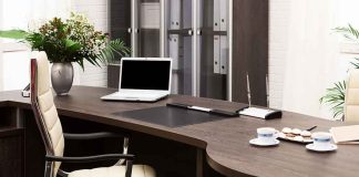 A modern office desk with a laptop, floral arrangement, and coffee cups