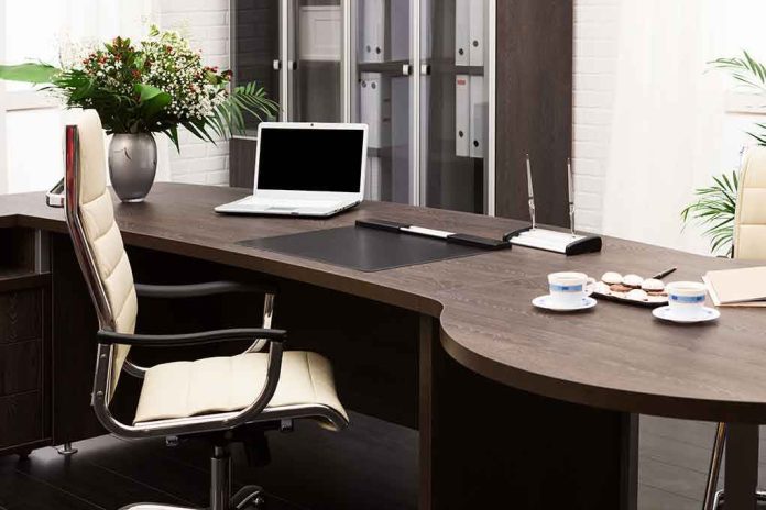 A modern office desk with a laptop, floral arrangement, and coffee cups