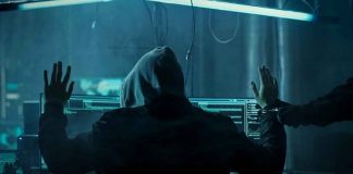 Hacker in hoodie arrested at computer desk.