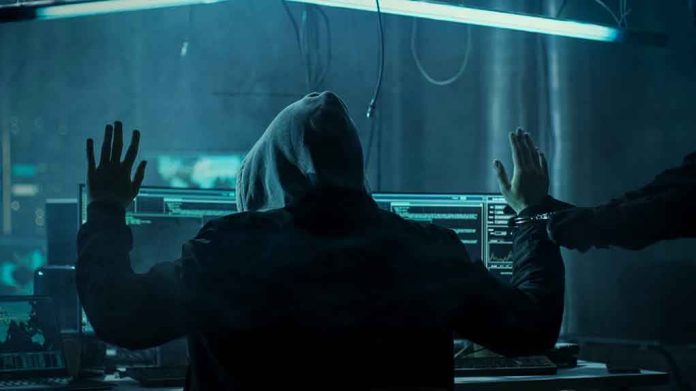 680075263 Hacker in hoodie arrested at computer desk.