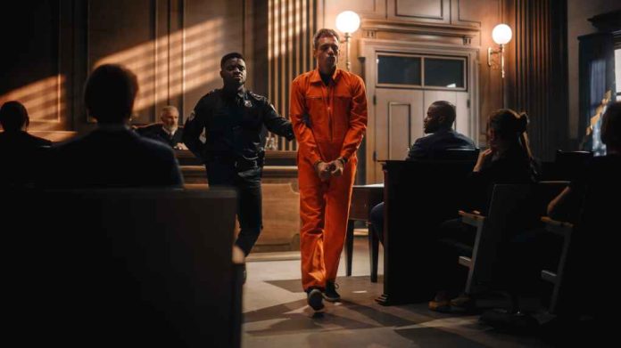 Justice-Trial-Proceedings_2056444856-1 Defendant in orange jumpsuit being escorted by a police officer in a courtroom