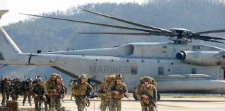 Soldiers disembark and walk past a large military helicopter