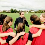 Camera Creep Called Out Coach talks to youth team in a huddle on a field