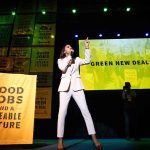 Speaker in white suit on stage at climate rally