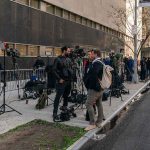 news crews set up cameras on a city sidewalk outside a courthouse
