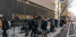 news crews set up cameras on a city sidewalk outside a courthouse