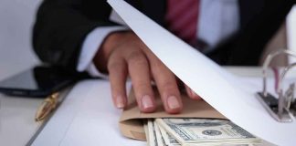 Businessperson hides cash in an envelope under documents
