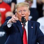 Trump Blasts Pirro Over Reflecting Pool Flip Man in suit pointing, speaking at a rally.