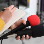 Trump Orders Major Changes to Childhood Vaccine Schedule Journalist holding two microphones while writing in a notebook