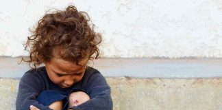 child sitting on ground with arms wrapped around knees