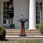 Trump’s Stone Age Promise Sparks War Jitters Podium with presidential seal in a garden colonnade