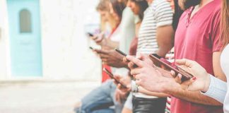 Group of people using smartphones while standing in a row